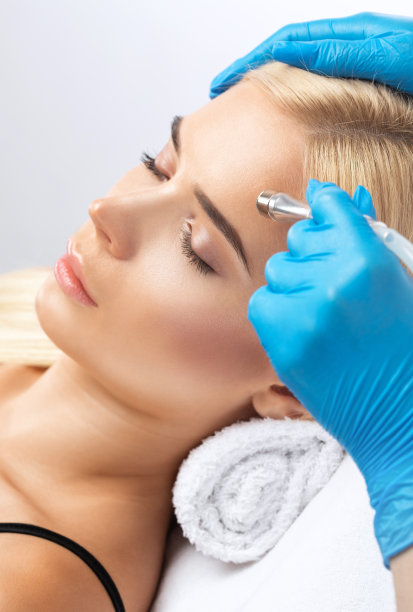 美容师在美容院为一位美丽的年轻女子做面部皮肤的微晶磨皮手术。美容及专业护肤。图片下载