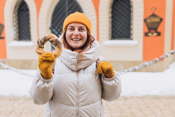在克拉科夫的市场广场上，戴着黄色帽子的年轻迷人女游客拿着传统的波兰百吉饼椒盐卷饼。冬天在欧洲旅行。高质量照片图片下载