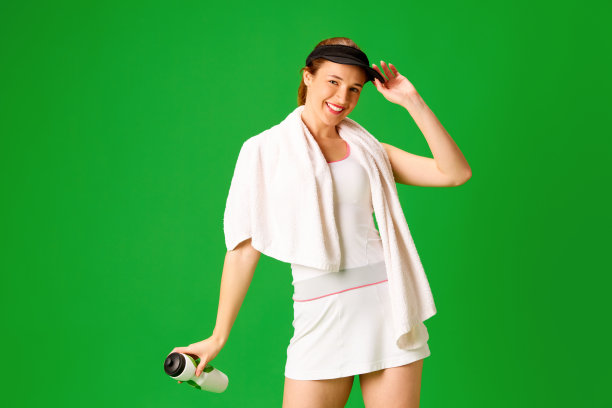 微笑，积极，快乐的年轻女孩穿着运动服，网球运动员站在绿色的工作室背景图片下载