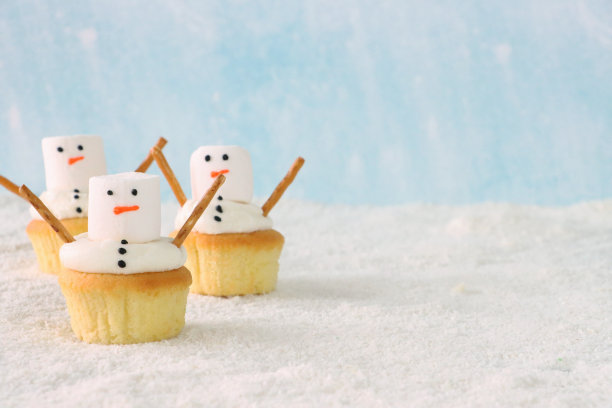 三，自制，雪人设计纸杯蛋糕的特写图片，白色的奶油漩涡装饰着大的白色棉花糖和咸椒盐卷饼棒手臂，冰糖雪，淡蓝色背景，重点在前景，复制空间图片下载