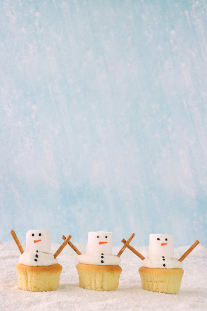 图片一排三个，自制的，雪人设计的纸杯蛋糕，白色奶油漩涡装饰着大的白色棉花糖和咸椒盐卷饼棒手臂，糖雪，淡蓝色背景，重点在前景，复制空间图片下载