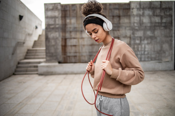 这是一位年轻的女运动员在水泥墙旁摆姿势的照片，她结束了跳绳的运动训练图片下载