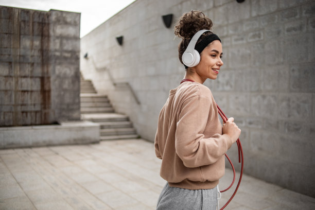 这是一位年轻的女运动员在水泥墙旁摆姿势的照片，她结束了跳绳的运动训练图片下载