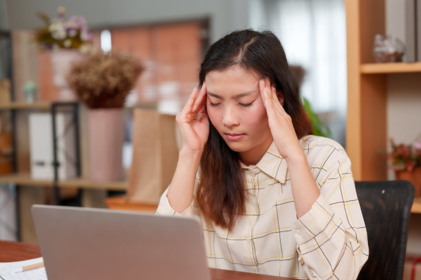 一个漂亮的亚洲办公室职员的中景照片。在笔记本电脑前工作时压力过大。因为紧张头疼，就用手按摩头部。坐在办公室里图片下载