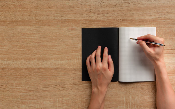 俯视图，男性用钢笔在木桌上的黑色笔记本上书写图片下载