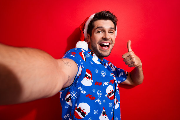 照片乐观的牙齿喜气小伙子戴圣诞帽印花衬衫看折扣空空间孤立在生动的红色背景图片下载