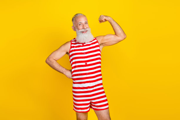 照片中酷酷强壮的老年男子穿着红色条纹泳衣，露出手臂肌肉孤立的黄色背景图片下载