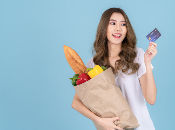 一名亚洲妇女从超市拎着一个纸购物袋，里面装着蔬菜图片下载