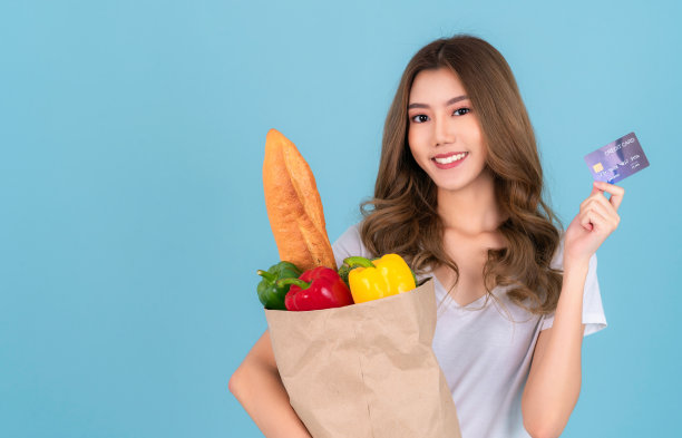 一名亚洲妇女从超市拎着一个纸购物袋，里面装着蔬菜图片下载