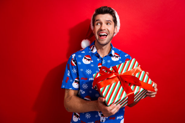 照片肖像时髦的年轻人拿着礼盒看空空间穿着圣诞老人印刷圣诞服装孤立的红色背景图片下载