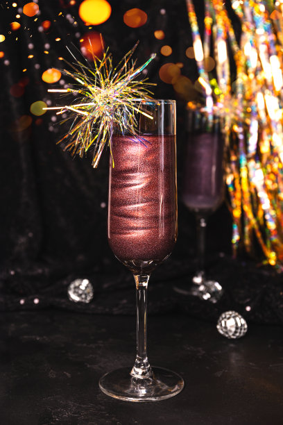 一杯新年鸡尾酒，黑色背景上有可食用的闪光，垂直照片图片下载