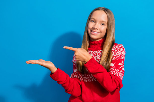穿着红色毛衣的迷人女学生的照片，在手掌上指示物体在蓝色背景上孤立的空白空间图片下载