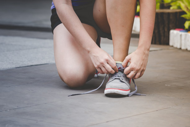 年轻女子跪下来系鞋带。在运动锻炼中准备跑鞋慢跑者。近距离的手绑跑步者的鞋带在健身房健康的人的生活方式。图片下载
