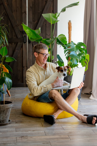 带着狗和笔记本电脑的时尚男士坐在家里的软椅上图片下载