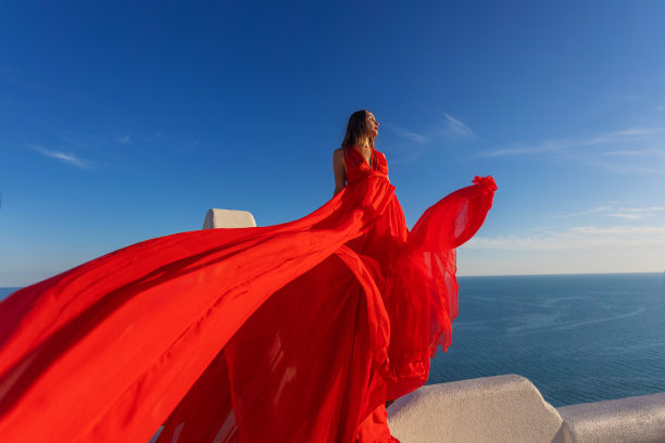 魅力的照片。女孩在大海的背景下挥舞着一件飘逸的红色连衣裙图片下载