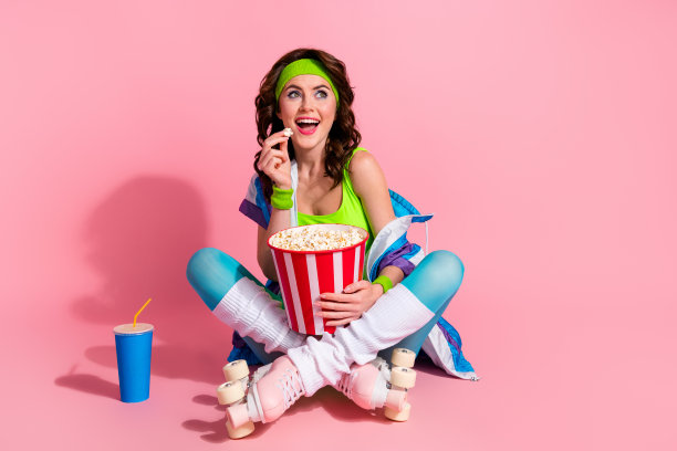 有趣的运动女教练坐在地板上吃爆米花的照片，在运动比赛广告上看空了空间，孤立的粉彩背景图片下载