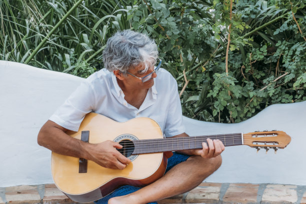 迷人的白发男子在他的乡间别墅弹吉他。图片下载