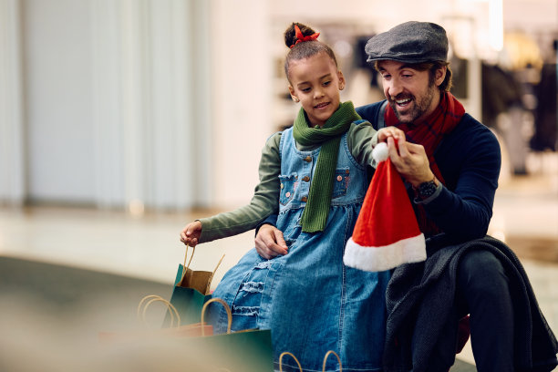 快乐的父亲和他的黑人女儿在购物中心买圣诞老人帽。图片下载