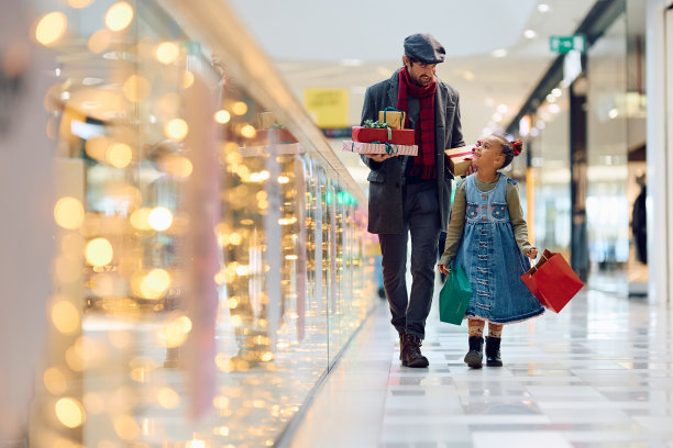 快乐的多种族父亲和女儿在圣诞节购物时穿过商场。图片下载