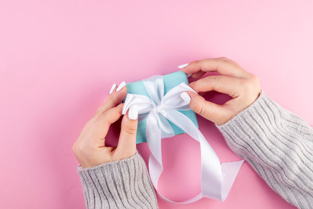第一人称俯视图照片的女性手拿蓝色礼盒与白色丝带在粉红色的背景。我的手捧着一个淡蓝色的礼品盒图片下载