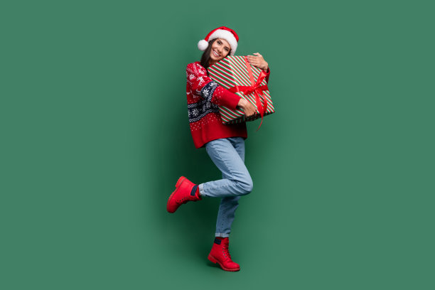 新年气氛的全身照片拥抱礼物礼盒圣诞老人车间快乐的圣诞女孩孤立的绿色背景图片下载