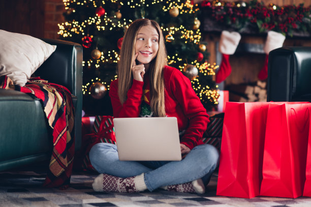 全尺寸的身体照片，年轻的十几岁的女孩使用电脑触摸脸颊看感兴趣的选择，认为最好的礼物在圣诞节期间的大型销售图片下载