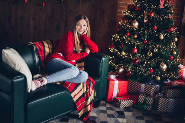 欢快可爱的十几岁女孩的全身照片享受平静的气氛，节日快乐的新年在圣诞树附近与礼物在室内图片下载