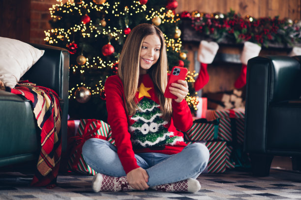 开朗的少女的全身尺寸照片，年轻的女孩牙齿灿烂，微笑着浏览智能手机，喜欢在家里为圣诞派对买礼物图片下载