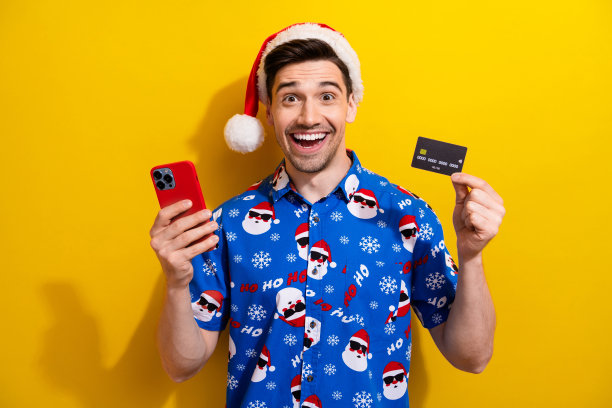 无现金服务男子的照片持有智能手机塑料信用卡兴奋的圣诞老人帽子网上商店孤立的黄色背景图片下载