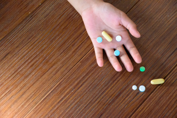 许多药片在手和木图案地板上俯视图不同颜色的片剂和胶囊表明药物和医疗的概念过量。图片下载