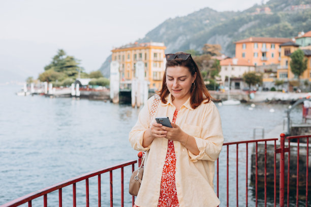 快乐的黑发女人享受暑假。假期和旅行的概念。Varenna,意大利。科莫湖。电话沟通。时髦女孩上网图片下载