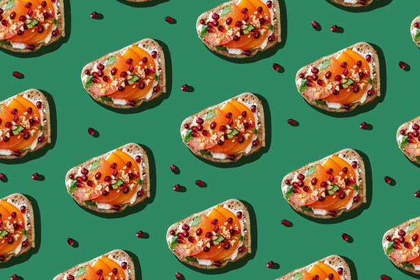 在绿色的背景上，烤面包配上奶油奶酪、柿子和石榴籽。创意美食照片概念图片下载
