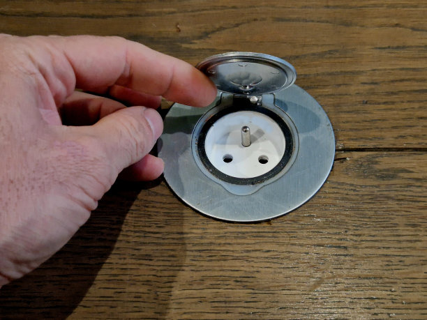 隐藏ip4插座在地面层。硬木地板。带有年轮纹理的木板和带有防水盖的灰色盖板，盖子。金属灰色圆形铰链连接，手开图片下载