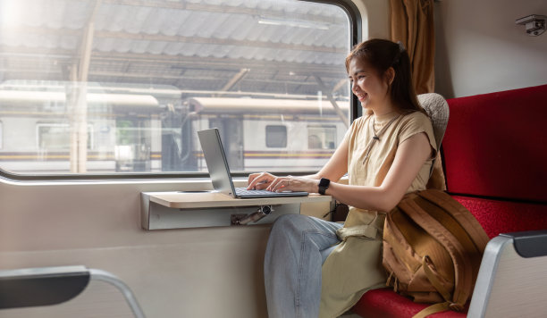 年轻的亚洲女子坐在火车上使用笔记本电脑。图片下载