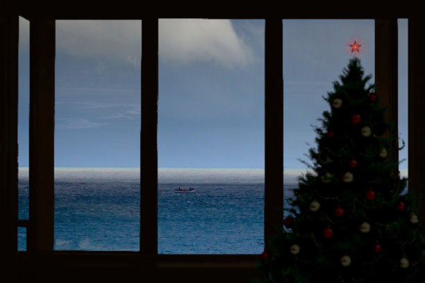 这是一幅蒙太奇照片，在窗户旁边有一棵圣诞树的剪影，背景是弗洛里亚诺波利斯海岸的景色，概念化了南半球国家的圣诞节庆祝活动。图片下载