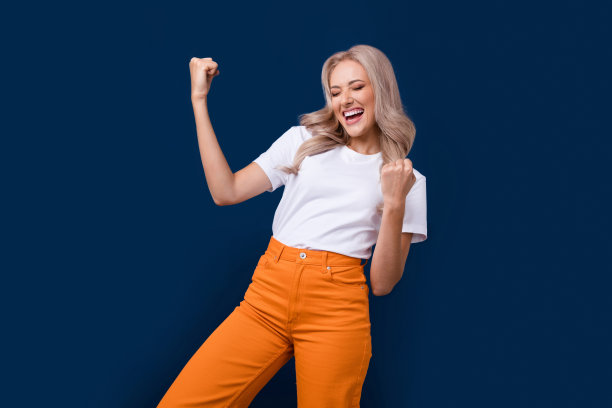 照片中快乐快乐的女孩穿着时髦的白色衣服，双手握拳庆祝胜利，孤立在深蓝色的背景下图片下载