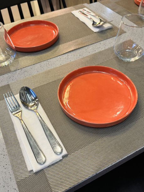 矩形餐桌的特写图片，餐具设置，橙色的餐盘放在材料的餐垫上，金属叉子和勺子放在餐巾纸上，高架的玻璃杯图片下载
