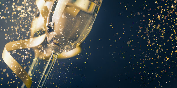 两个香槟酒杯，金色缎带和金色闪光飞溅散景在黑暗的背景。豪华餐厅晚宴庆典。经典的圣诞和新年假期全景设计横幅。图片下载