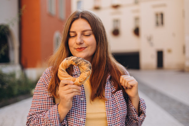 克拉科夫集市广场上，30多岁的年轻美女背着背包，手里拿着波兰传统小吃椒盐卷饼。春天去欧洲旅行。有选择性的重点。高质量照片图片下载