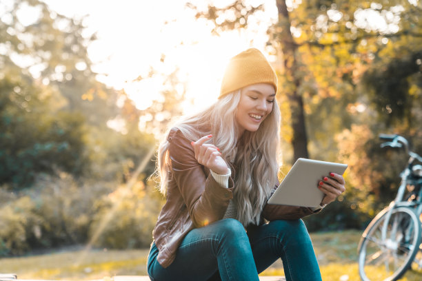 一个美丽的年轻微笑的女人在公园里用平板电脑上网图片下载