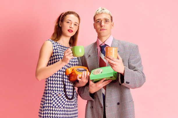 咖啡休息。年轻的男人和女人，员工，同事站在粉红色的工作室背景下，拿着杯子和手机图片下载