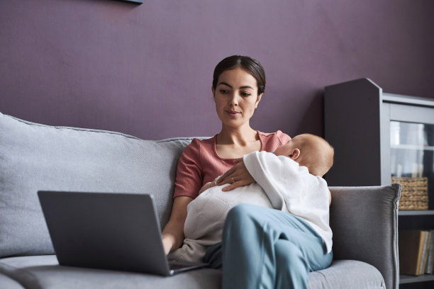 一名妇女抱着熟睡的婴儿使用笔记本电脑图片下载