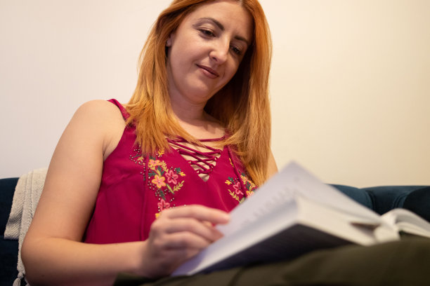 心满意足的姜色女人正在家里深蓝色的沙发上看书。库存图片图片下载