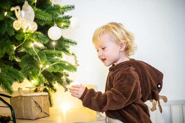 一个可爱的小男孩在家里装饰圣诞树的照片图片下载