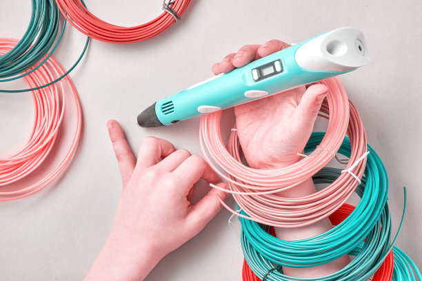 孩子的手与现代3D笔和许多塑料材料环在桌子上图片下载