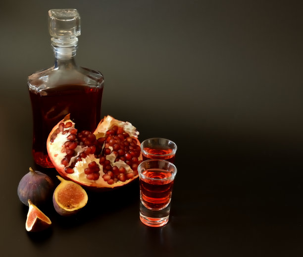 无花果石榴利口酒，黑色背景上的两杯一瓶自制酒，旁边是成熟的水果。图片下载