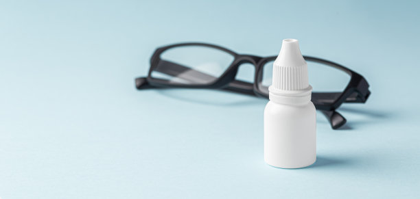 眼药水瓶与眼镜在蓝色背景图片下载