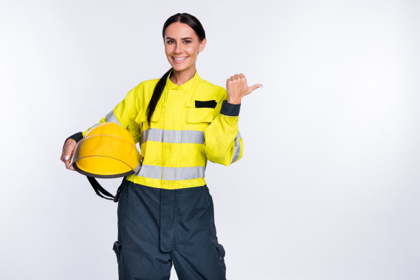 照片中快乐开朗的年轻女消防员戴着黄色的头盔，拇指指向空的空间孤立的白色背景图片下载