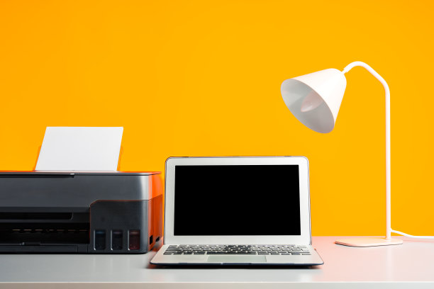 桌子上的激光打印机和笔记本电脑，黄色背景图片下载