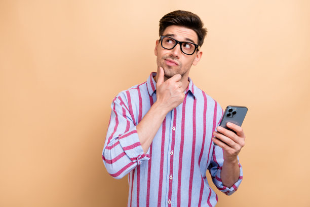 年轻的知识分子商人的照片思考触摸下巴时，使用智能手机孤立的米色背景看copyspace图片下载